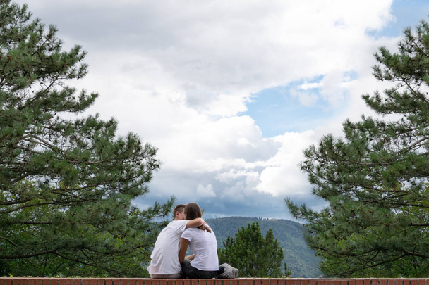 El tipo besa a una chica en el borde de un edificio alto en el fondo de las montañas
. - Foto, imagen