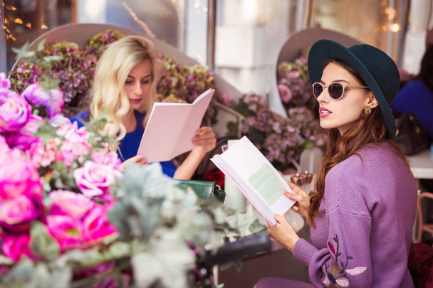Dwa piękne, eleganckie młodych kobiet siedząc przy stoliku w kawiarni na świeżym powietrzu i czytanie menu - Zdjęcie, obraz