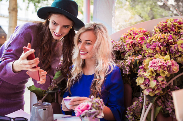 Two beautiful young women looking at the phone in the restaurant outdoor - Фото, изображение