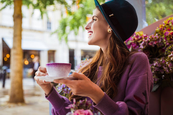 Side view of the elegant young woman who is sitting in the restaurant outdoor and drinking cup of tea - Foto, imagen