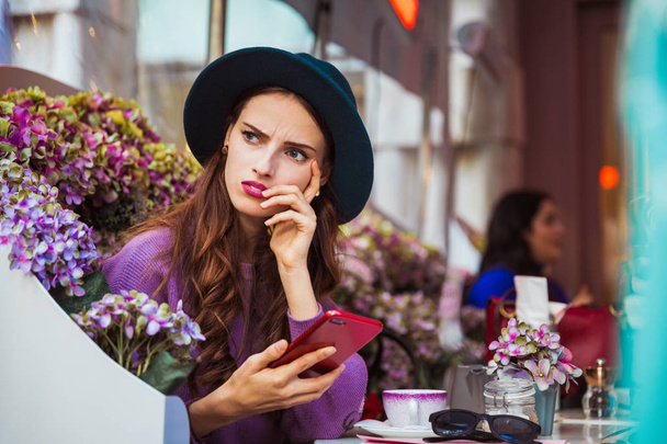 Portrait of the dissatisfied young woman who is sitting in the restaurant outdoor and looking aside - 写真・画像