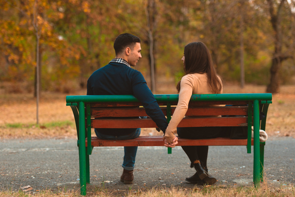 pár drží za ruku a sedí na lavičce v podzimním parku - Fotografie, Obrázek