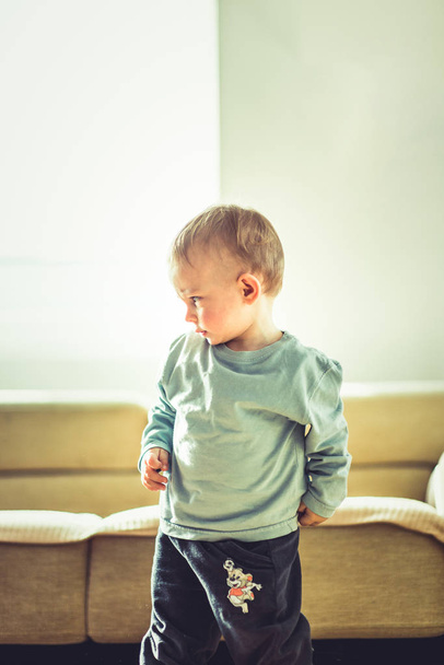 A little baby boy is standing in the living room and looking interested - Photo, image