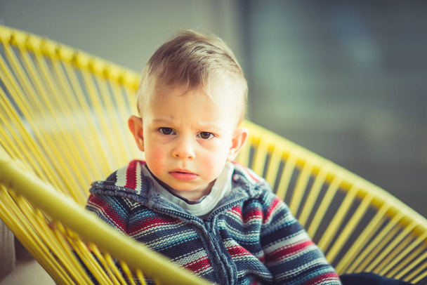 Angry baby boy is looking serious while sitting on the chair - 写真・画像
