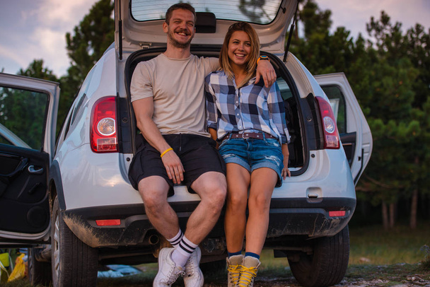 Giovane coppia seduta sul retro di un fuoristrada e godendo la vista dall'interno del veicolo all terrain al tramonto
. - Foto, immagini