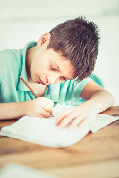 Un petit garçon est assis sur la table et écrit dans son carnet. - Photo, image