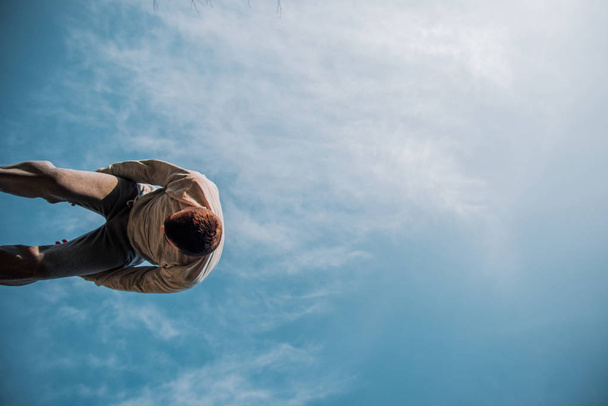 Homem caucasiano abaixo do céu azul fazer salto parkour
 - Foto, Imagem