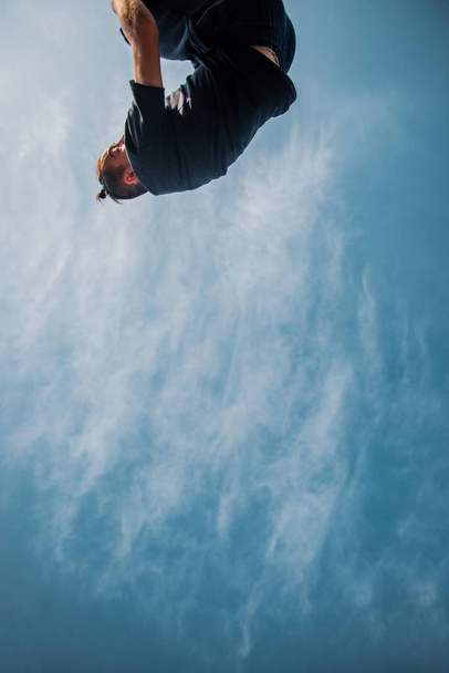 Corredor libre entrenamiento parkour mientras salta por debajo de las nubes blancas
 - Foto, Imagen