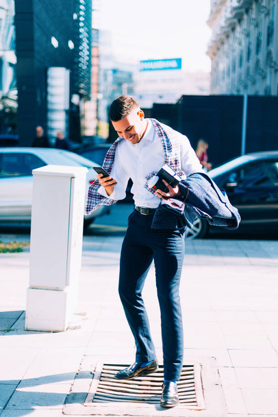 Бізнесмен стоїть на вулиці у вітряний день і цікавиться своїм мобільним телефоном
 - Фото, зображення
