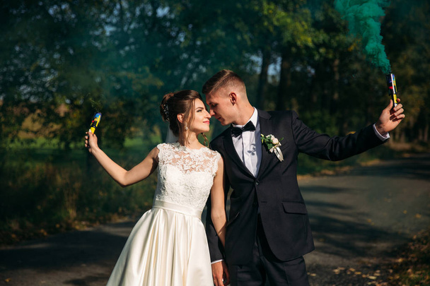 Весільна пара тримає кольоровий дим в руках посеред алеї
 - Фото, зображення