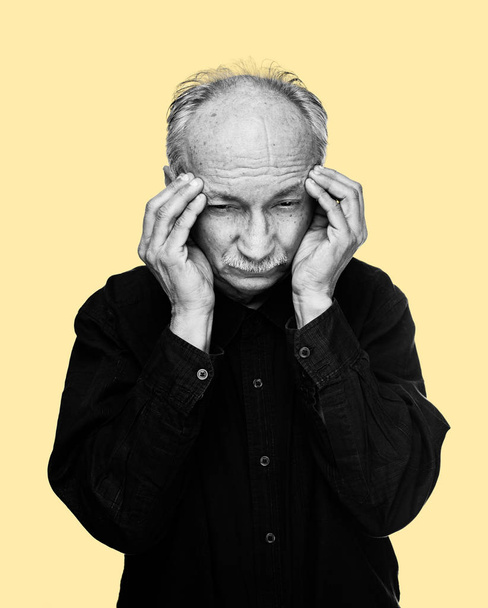 Gesundheitskonzept. Schwarz-Weiß-Bild eines alten Mannes mit Kopfschmerzen isoliert auf gelbem Hintergrund - Foto, Bild