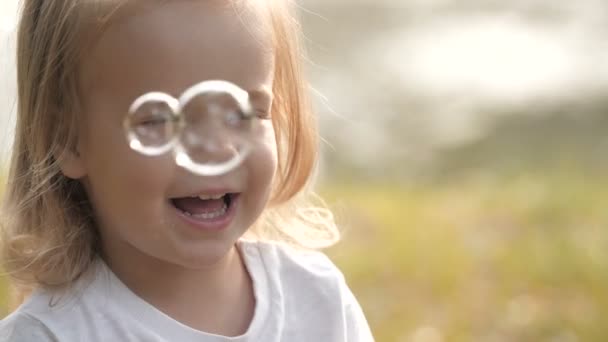 Retrato de bebé sonriente con burbujas de jabón mirando a la cámara en el parque de verano a la luz del atardecer
. - Metraje, vídeo