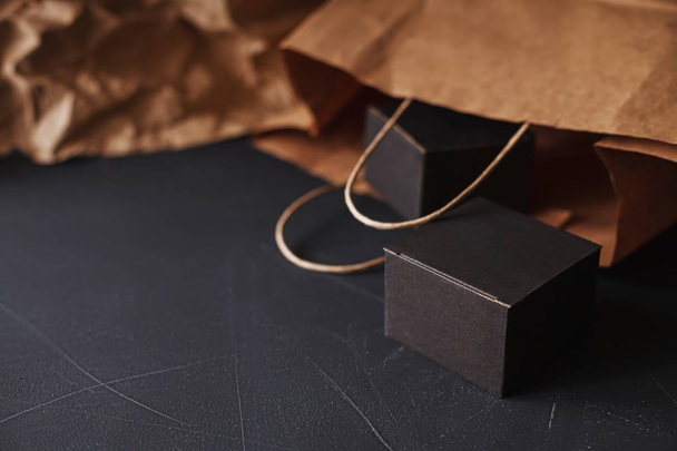 A fekete festett karmolt felszín szóló két matt fekete karton díszdobozok, kézműves papír zsák elmosódott a háttér, otthoni csomagolópapír kézműves téma - Fotó, kép