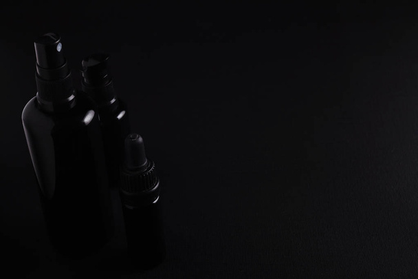 Set of three various luxury unbranded skin care product bottles made of black shiny glass on matte black canvas background  - 写真・画像