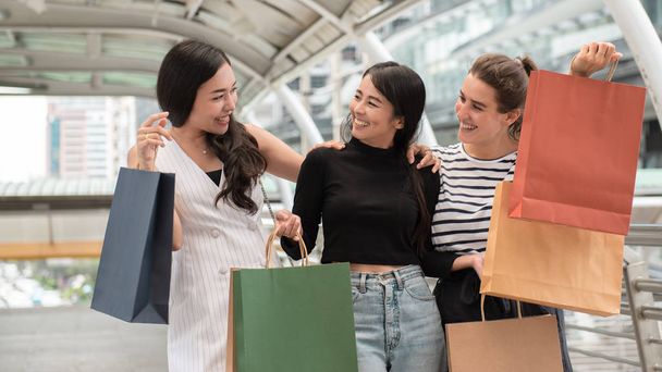 Счастливые друзья ходят по магазинам. Три красивые молодые женщины наслаждаются покупками в городе
. - Фото, изображение
