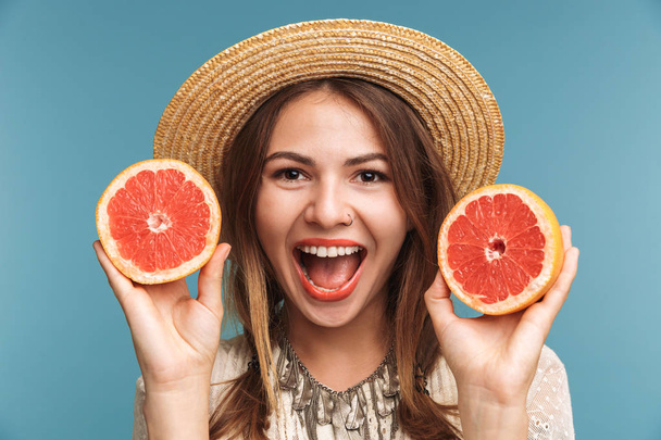 Image of a happy pretty woman posing isolated over blue wall background with orange citrus. - Valokuva, kuva