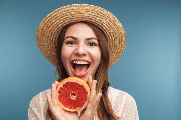 Image of a happy pretty woman posing isolated over blue wall background with orange citrus. - Photo, image