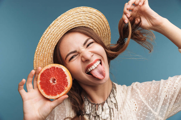 Image of a happy pretty woman posing isolated over blue wall background with orange citrus. - Фото, зображення