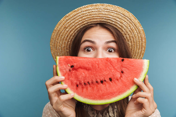 Image of a shocked pretty woman posing isolated over blue wall background with watermelon covering face. - Photo, image
