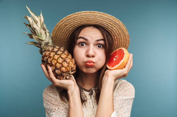 Image of cute funny young beautiful woman isolated over blue wall holding citrus and pineapple. - Fotoğraf, Görsel