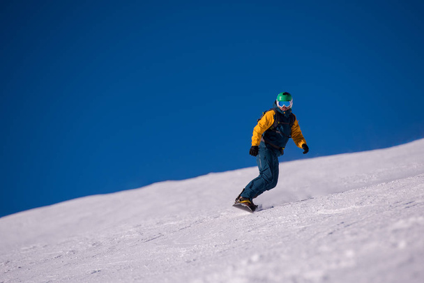 Young freestyle snowboarder running down the slope and ride free style at sunny winter day on Alpine mountains. Winter sport and recreation, leisure outdoor activities. - Photo, image