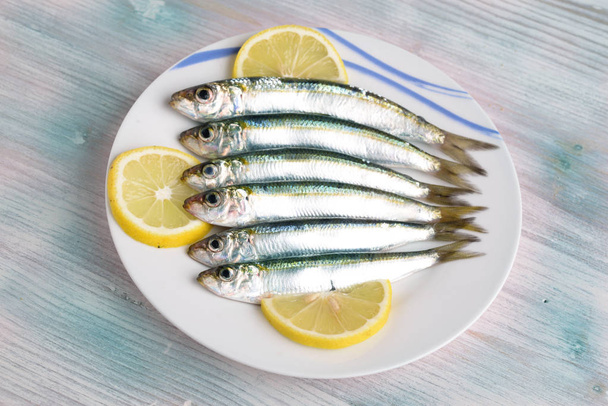 Sardinen mit Zitronenkeilen und Petersilie auf Teller mit farbigem Holzhintergrund - Foto, Bild