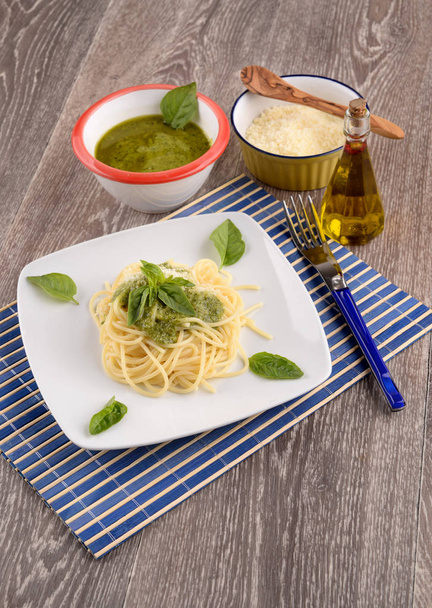 Placa de espaguetis con pesto y hojas de albahaca sobre la mesa
 - Foto, imagen
