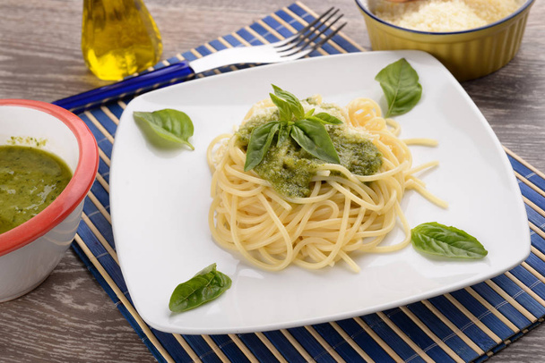 Teller Spaghetti mit Pesto und Basilikumblättern auf dem Tisch - Foto, Bild
