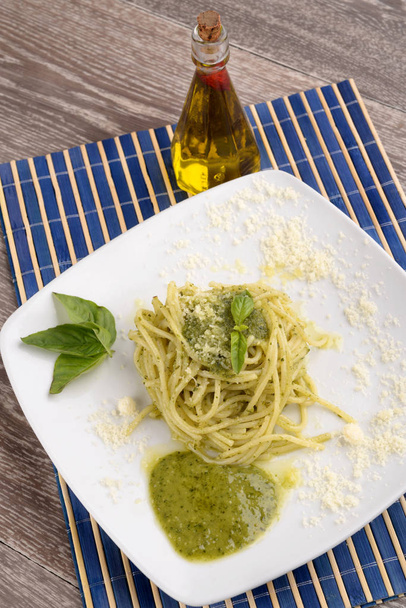 Piatto di spaghetti al pesto e foglie di basilico in tavola
 - Foto, immagini