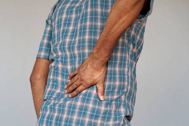 Nahaufnahme eines Afrikaners mit Nierenschmerzen, isoliert auf grauem Hintergrund. Ein älterer Mann mit Rückenschmerzen umklammert ihre Hand am unteren Rücken. Mann leidet unter Rippenschmerzen, Bauchschmerzen. - Foto, Bild
