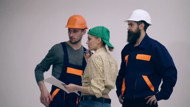 Three builders are discussing the construction plan. Concept of construction works. Woman and two men in helmets are considering a construction plan. - Felvétel, videó