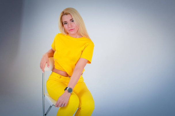 White to light blue gradient background. Model girl sitting on a chair with her head bent in a yellow shirt in yellow tones. - Fotografie, Obrázek