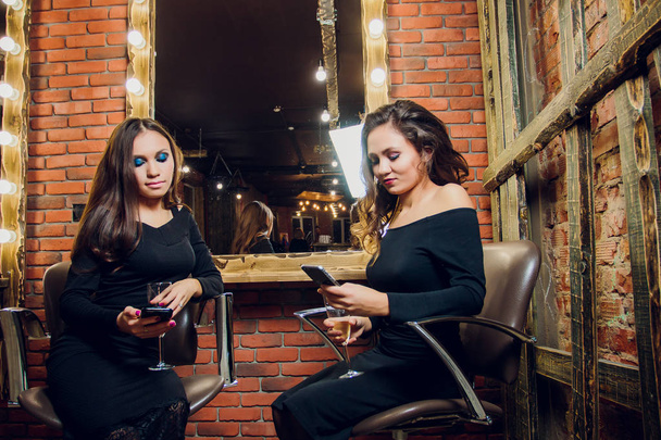 Two beautiful young woman outside at a city cafe laughing and drinking champagne. - 写真・画像