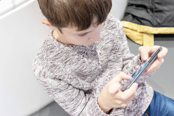 A boy sitting in the mall and hanging a smartphone. - 写真・画像