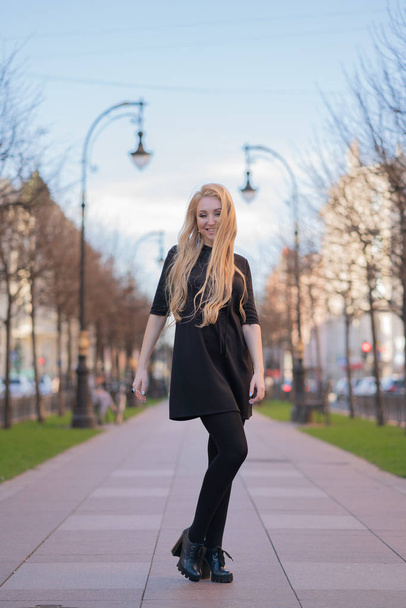 素敵な金髪女性の市松模様ベージュ スカーフと革のジャケット、黒のドレスで街を歩くし、積極的に人生を楽しんでいます - 写真・画像