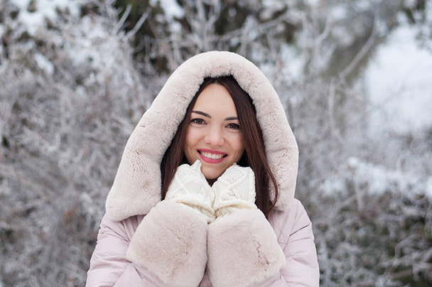 Портрет молодой красивой эмоциональной женщины в капюшоне и перчатках на заснеженном фоне сада. Зимний снежный пейзаж
 - Фото, изображение