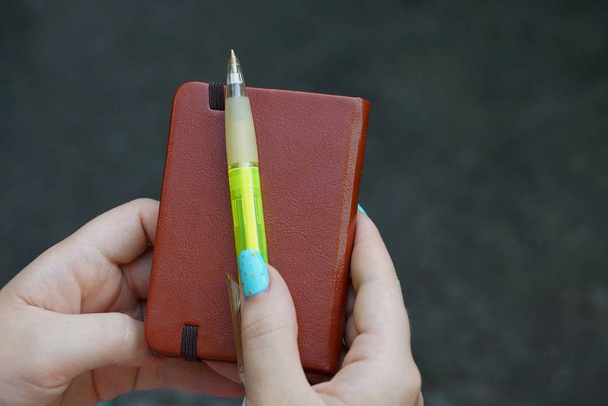 Caderno fechado marrom e caneta verde nas mãos
 - Foto, Imagem