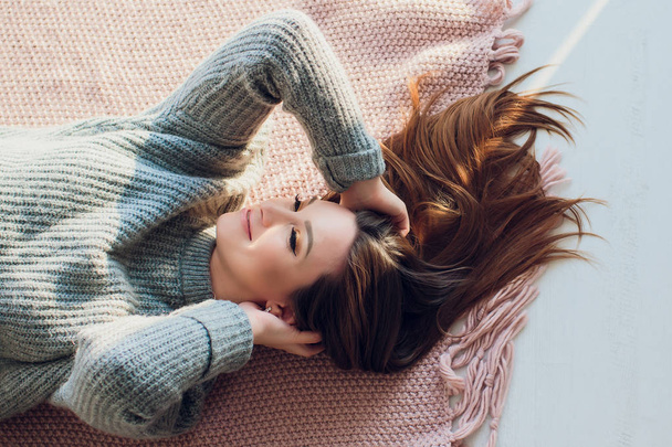 Beautiful sexy tan brunette woman posing in bedroom, wearing cozy grey sweater and knitted socks. Rest, sleeping, comfort concept. Close up of young woman lying in bed at home. Scandinavian home. - Foto, Imagem