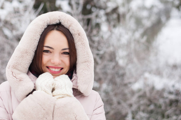 Portrait de jeune belle femme émotionnelle en manteau à capuchon et gants sur fond de jardin enneigé. Paysage enneigé d'hiver
 - Photo, image