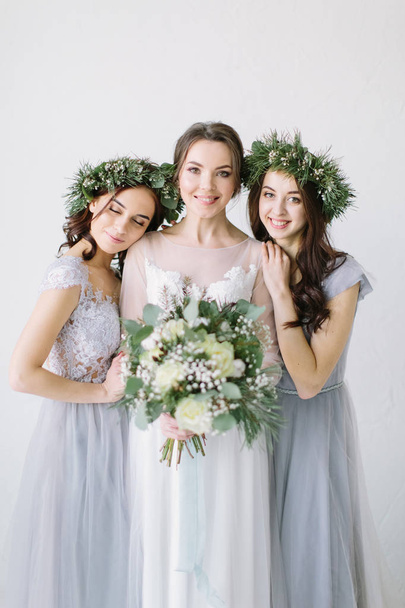 Beautiful laughing bride in a white wedding dress holding bouquet with bridesmaids in blue grey dresses and wreathes - Photo, image