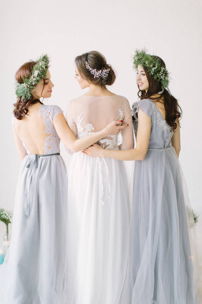 Bride standing with her back in a white wedding dress with two bridesmaids in blue dresses - Foto, imagen