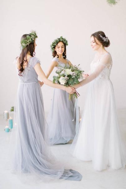 Bride and bridesmaids holding hands and dancing in white studio. Full-lenght portrait - 写真・画像