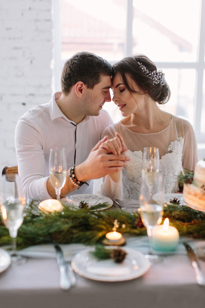Menyasszony és a vőlegény a fehér terem díszített asztal pózol. Kéz a kéz. Élvezze a pillanatot a boldogság és a szeretet. Egy fotósorozat tárcámhoz. Esküvői virágok az asztalra - Fotó, kép