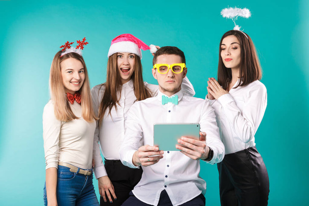 新しい年のテーマ クリスマス冬事務所社員。グループ 4 若い白人の人々 ビジネス笑顔休日面白い帽子アクセサリー メガネ写真を撮る自分 selfie タブレット ブルー背景 - 写真・画像