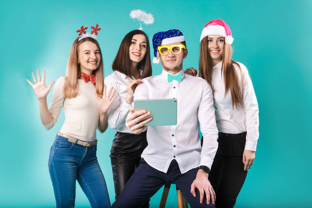 Thème Nouvel An Noël hiver employés de l'entreprise de bureau. Groupe 4 jeunes Caucasiens gens d'affaires sourire vacances drôles chapeaux accessoires lunettes prendre photo vous-même selfie tablette fond bleui
 - Photo, image