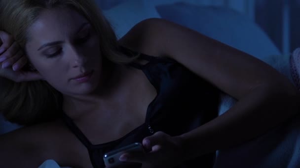 Woman reading unpleasant message from boyfriend, lying in bed alone, sadness - Кадри, відео