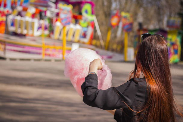 Jovem de pé com algodão rosa doce p no parque de diversões
 - Foto, Imagem