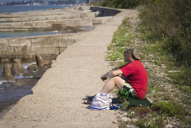 Ένας άνδρας κάθεται σε τοίχο ενίσχυση στην ακτή της Μαύρης Θάλασσας. - Φωτογραφία, εικόνα