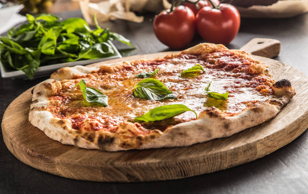 Italian traditional pizza margarita on round wooden board with basil tomatoes and parmesan. - Foto, afbeelding
