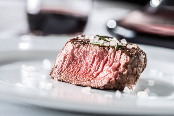 Beef tenderloin steak on white plate and red wine in pub or restaurant. - Фото, изображение